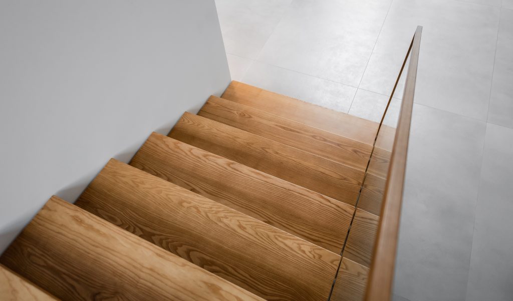 Wooden Staircase In A Building. Empty Downwards Staircase With White Walls. Photo Of Seven Wooden Steps In Warm Tones.